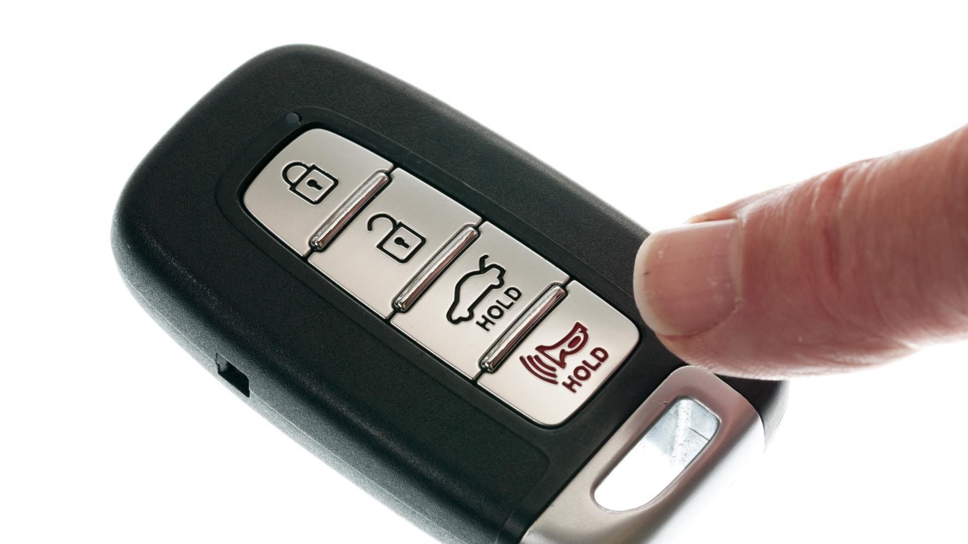 A close-up of a hand holding and examining a car key fob, representing the first step in programming a remote car starter.