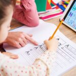 A dedicated teacher assists a young student in writing the letter 'A' on a worksheet, fostering early literacy skills in an after school program.