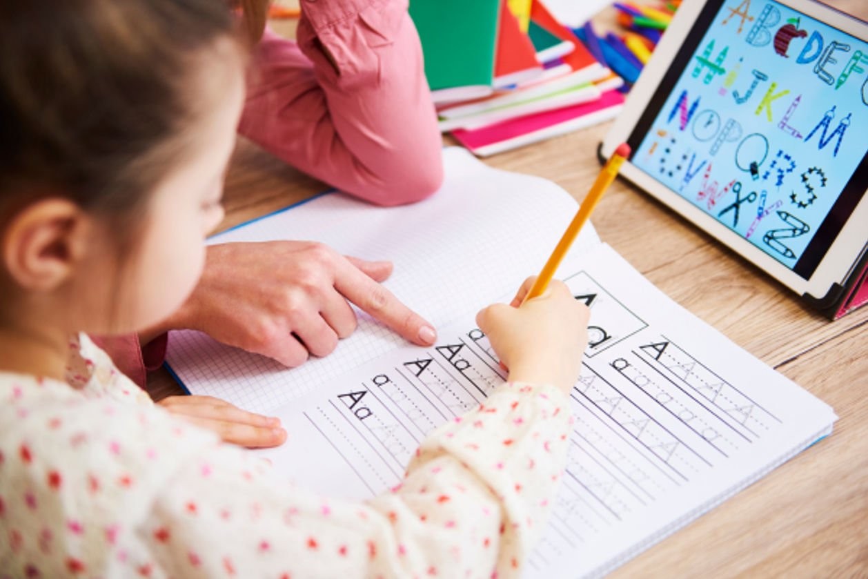 A dedicated teacher assists a young student in writing the letter 'A' on a worksheet, fostering early literacy skills in an after school program.