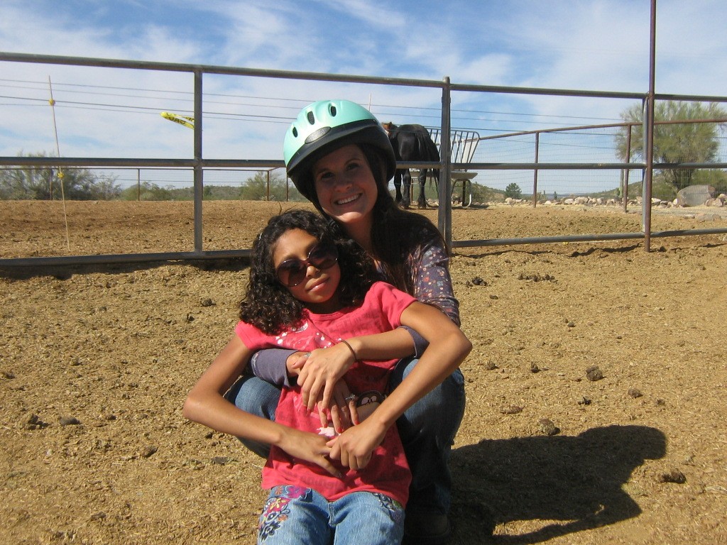 Two smiling women, one adult and one child, sitting closely together and looking at each other, representing the positive relationship in a foster care mentor program.