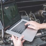 Car computer reprogramming process being performed by a mechanic using a diagnostic scanner connected to a car's OBD-II port to update the engine control module software for improved vehicle performance and efficiency.