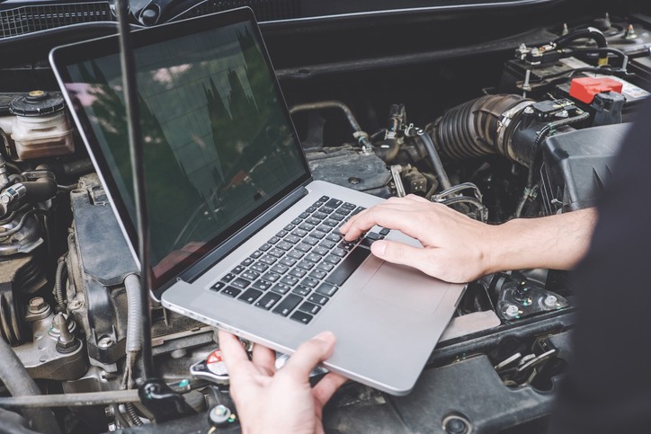 Automotive technician using diagnostic tool for car computer reprogramming to update engine control module software.