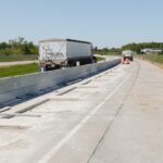 Construction underway on a highway segment for wireless electric vehicle charging tests as traffic flows by.