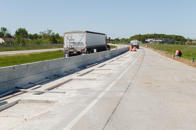 Construction underway on a highway segment for wireless electric vehicle charging tests as traffic flows by.