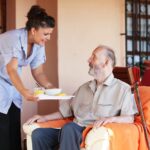 A caregiver brings a meal to a senior in their home, illustrating the concept of home care for the elderly.