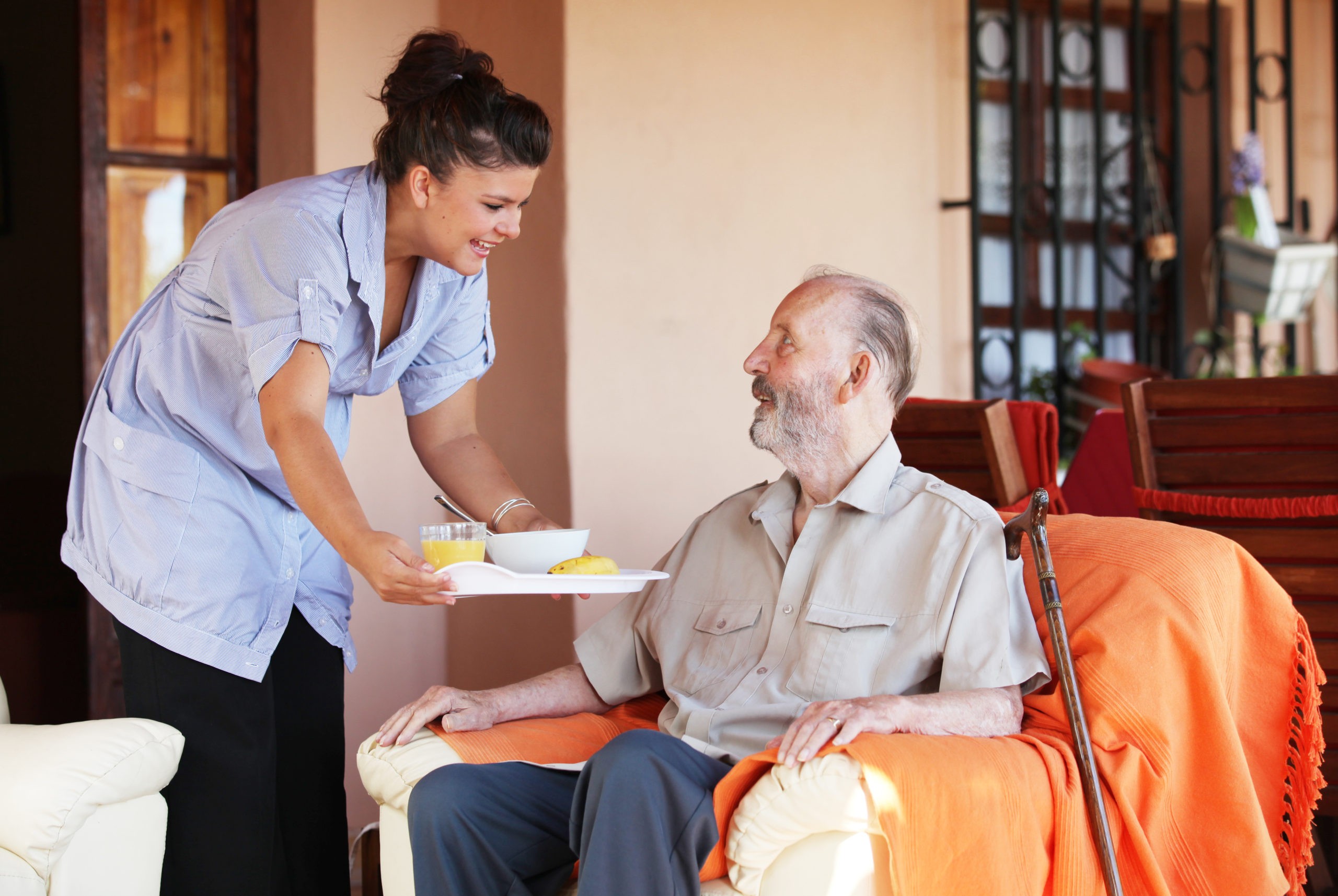 A caregiver brings a meal to a senior in their home, illustrating the concept of home care for the elderly.