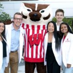 Students in their white coats pose with Bucky Badger