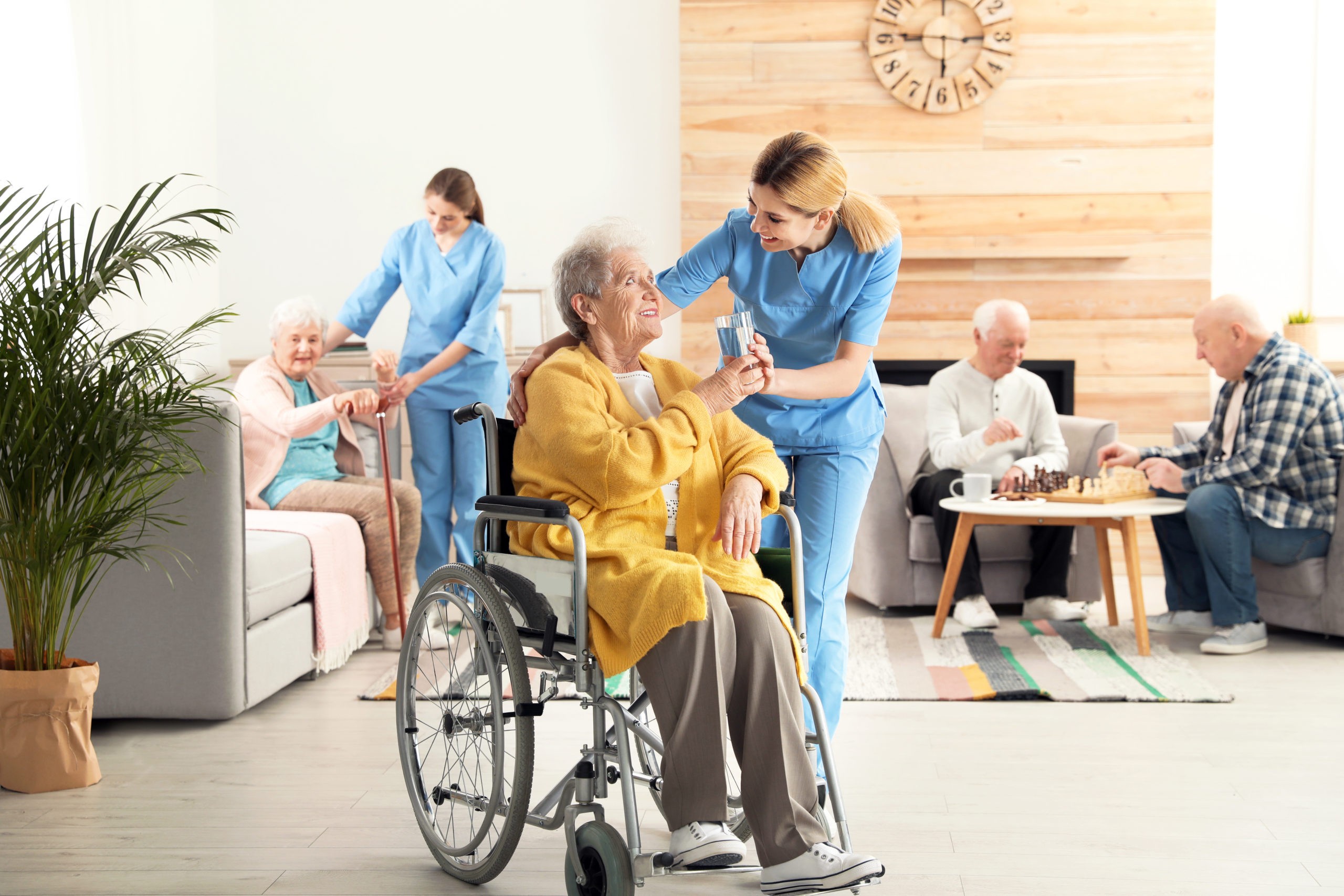 Elderly care at home, featuring a smiling senior woman in a wheelchair being offered water by a nurse, highlighting assistance for senior people