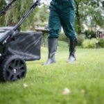 A close up of a person mowing a lawn.