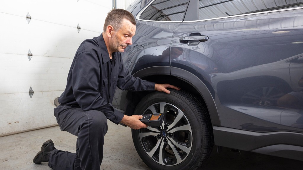 Automotive technician using a TPMS diagnostic scan tool to perform a tire pressure monitoring system relearn procedure on a vehicle, highlighting the importance of proper TPMS maintenance.