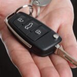 Hand holding a Ford key fob and car key, illustrating Ford key fob programming for keyless entry.