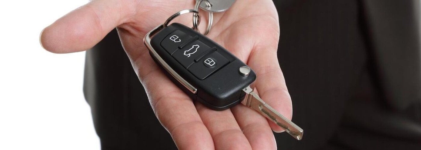 Hand holding a Ford key fob and car key, illustrating Ford key fob programming for keyless entry.